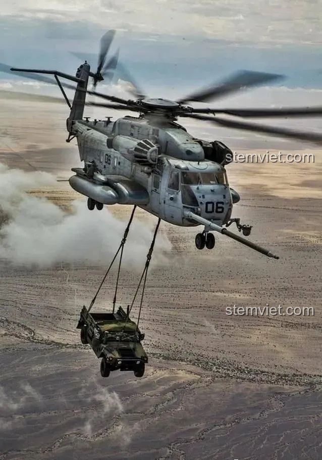 Hình ảnh thực tế trực thăng vận tải hạng nặng CH-53E Super Stallion đang bay trên sa mạc, cẩu một chiếc xe quân sự.