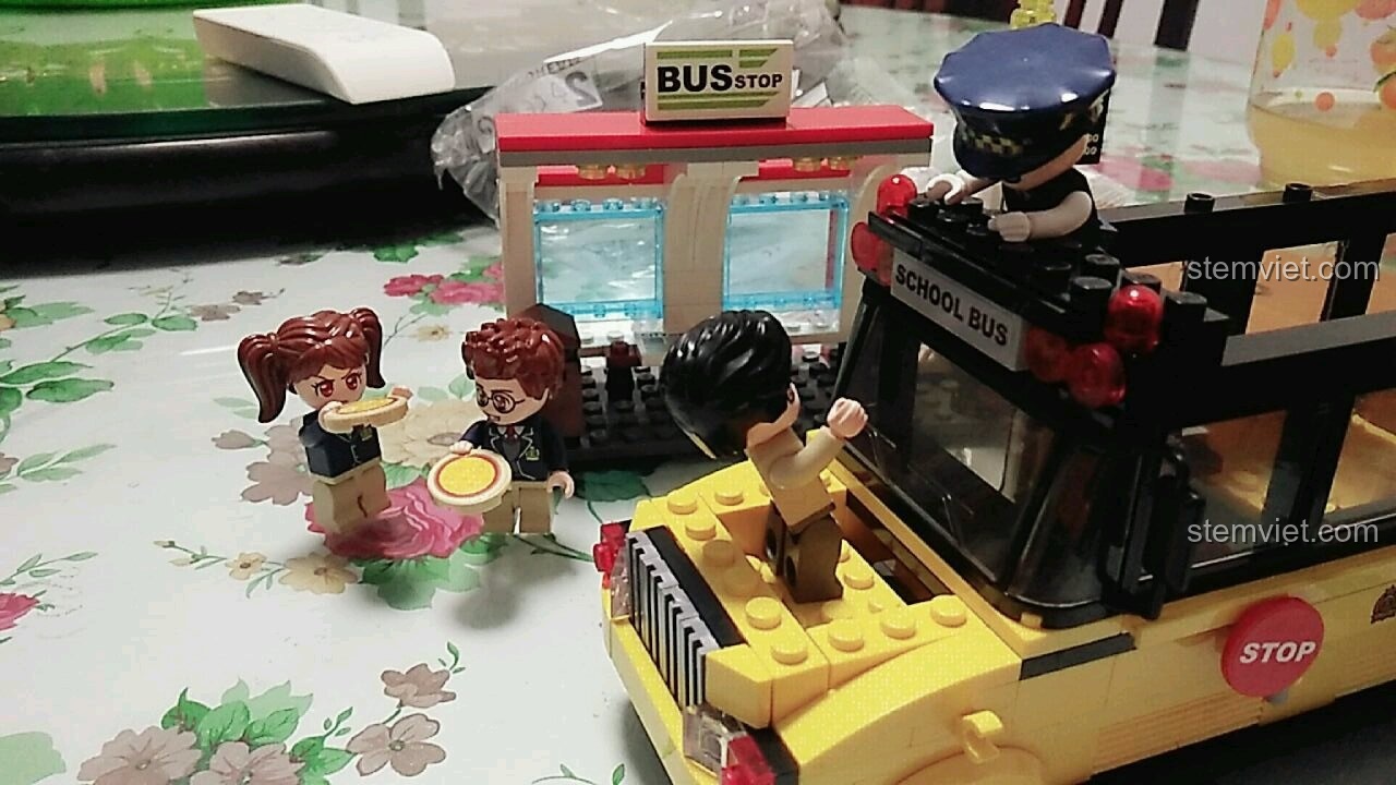 Bác tài xế và cô giáo đang hoàn thiện xe buýt trường học, trong khi các học sinh đã ăn xong pizza và chờ đợi trong bộ QMAN 1136.