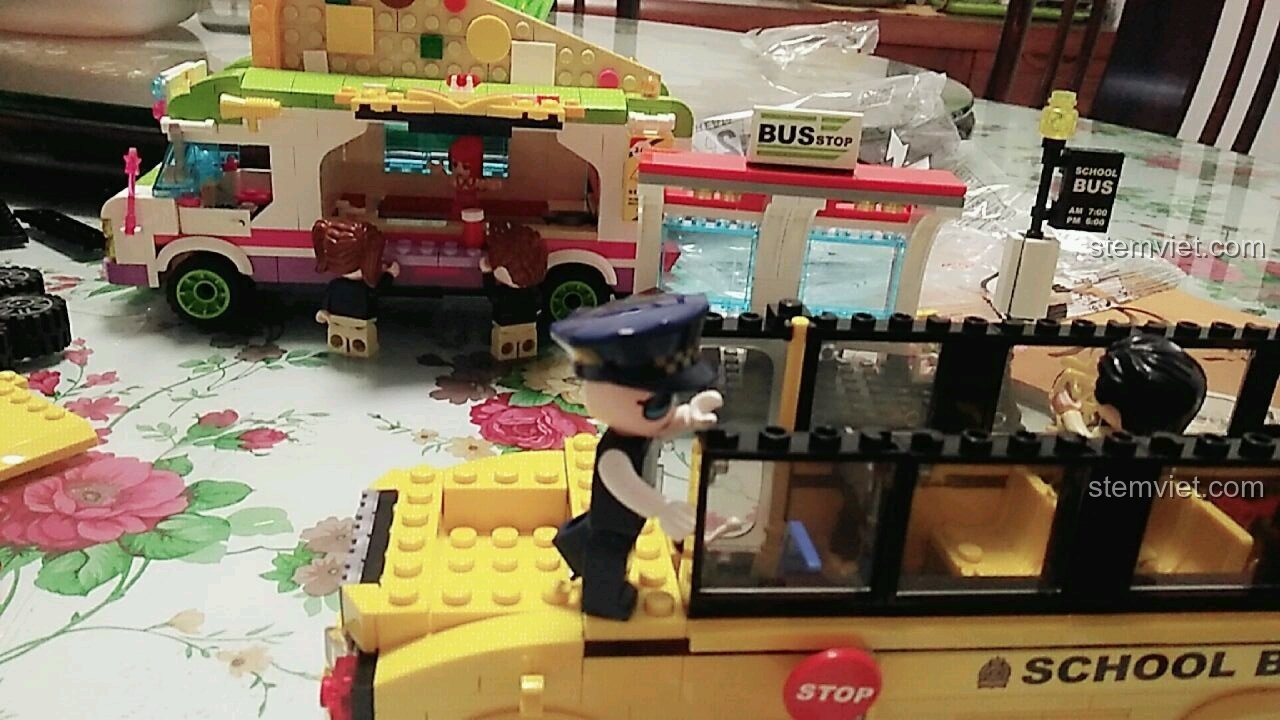 Các học sinh đang mua pizza từ một xe bán hàng lưu động, trong khi xe buýt trường học QMAN 1136 đang được lắp ráp.