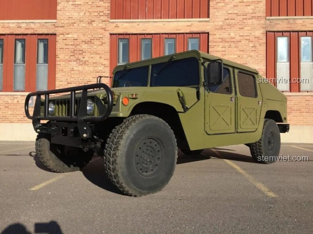 Chiếc Humvee H1 quân sự màu xanh lá cây đậu trên nền gạch và đường kẻ vàng.