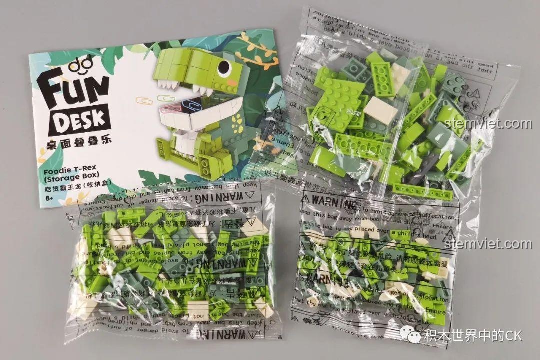 Ảnh unboxing bộ đồ chơi lắp ráp hộp đựng đồ khủng long T-Rex JAKI Fun Desk, hiển thị các túi mảnh ghép và sách hướng dẫn.