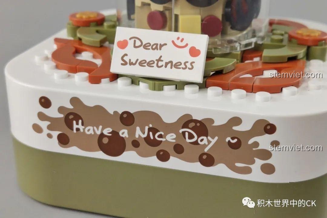 Cận cảnh phần đế của hộp nhạc trà sữa JAKI với dòng chữ 'Have a Nice Day' và 'Dear Sweetness' được in trên bề mặt.