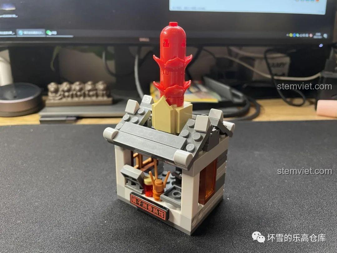 Mô hình quán Lạp Xưởng Đảo Quýt JAKI JK2131 với kiến trúc mái ngói cổ kính và cây lạp xưởng khổng lồ trên mái.