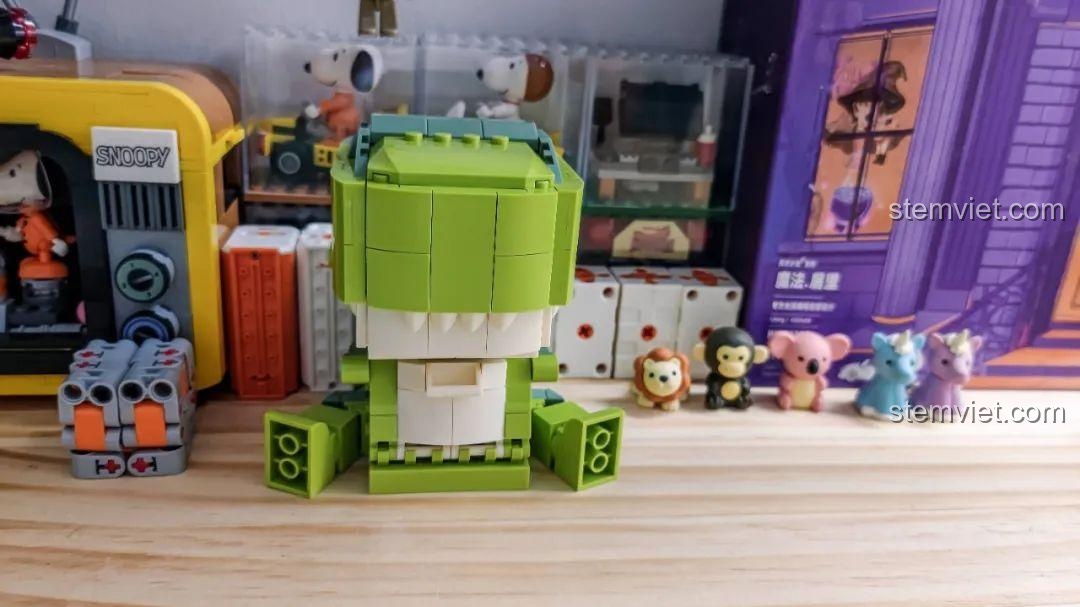 Mô hình Khủng long T-Rex trang trí JAKI JK5102 trên kệ gỗ cùng các mô hình động vật nhỏ khác, tạo không gian vui nhộn.