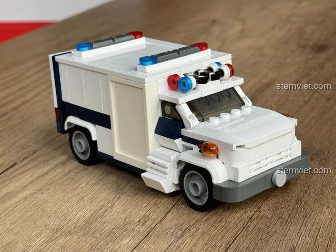 Mô hình xe cứu thương JAKI JK9211 đã hoàn thiện, nhìn từ góc 3/4 phía trước bên trái, với đèn còi đặc trưng.