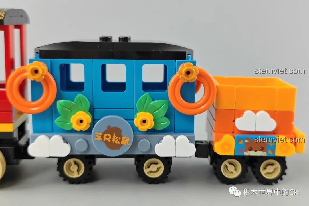 Cận cảnh toa hành khách màu xanh của tàu JAKI, có logo 'Ba Chú Sóc', các chi tiết hoa lá và đám mây được in sắc nét.