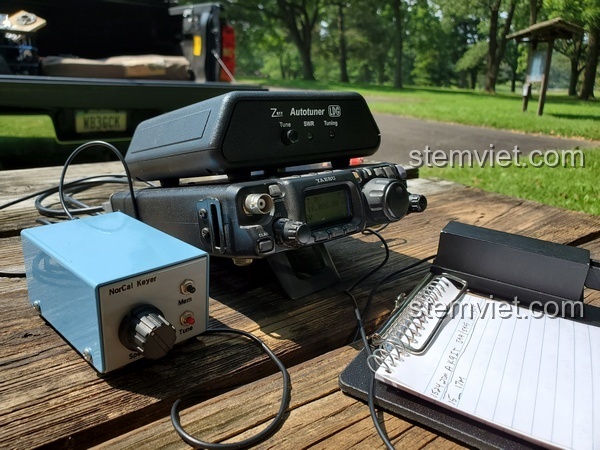 Mô hình Radio dã chiến FT-817 từ Jisi 817 được đặt trong một không gian làm việc ngoài trời, thể hiện tính di động.