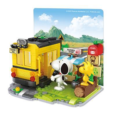 Mô hình Peanuts Snoopy: School Bus với xe buýt màu vàng, Snoopy và Woodstock trên nền cảnh quan núi non và biển báo giao thông, có cửa hàng hoa và hộp thư.