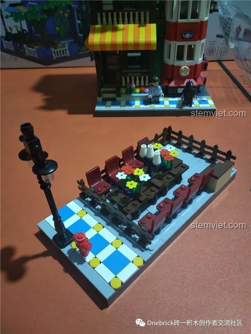 Khu vực ăn uống ngoài trời của bộ WANGE 6313, với bàn ghế, hàng rào, hoa và cột đèn đường.