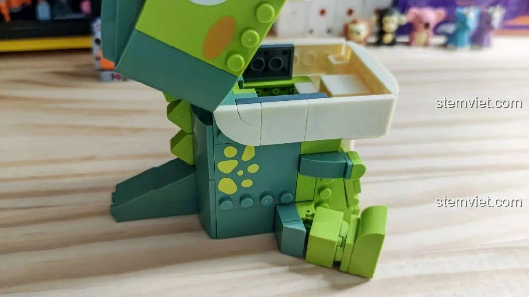 Khủng long T-Rex trong bộ JAKI JK5102 đang 'ăn' một cây bút, minh họa chức năng hộp đựng bút.