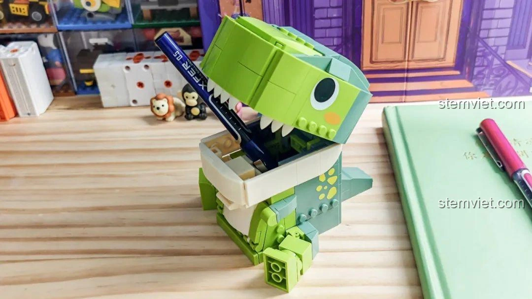 Khủng long T-Rex trong bộ JAKI JK5102 đựng hai cây bút, minh họa sức chứa của hộp đựng.