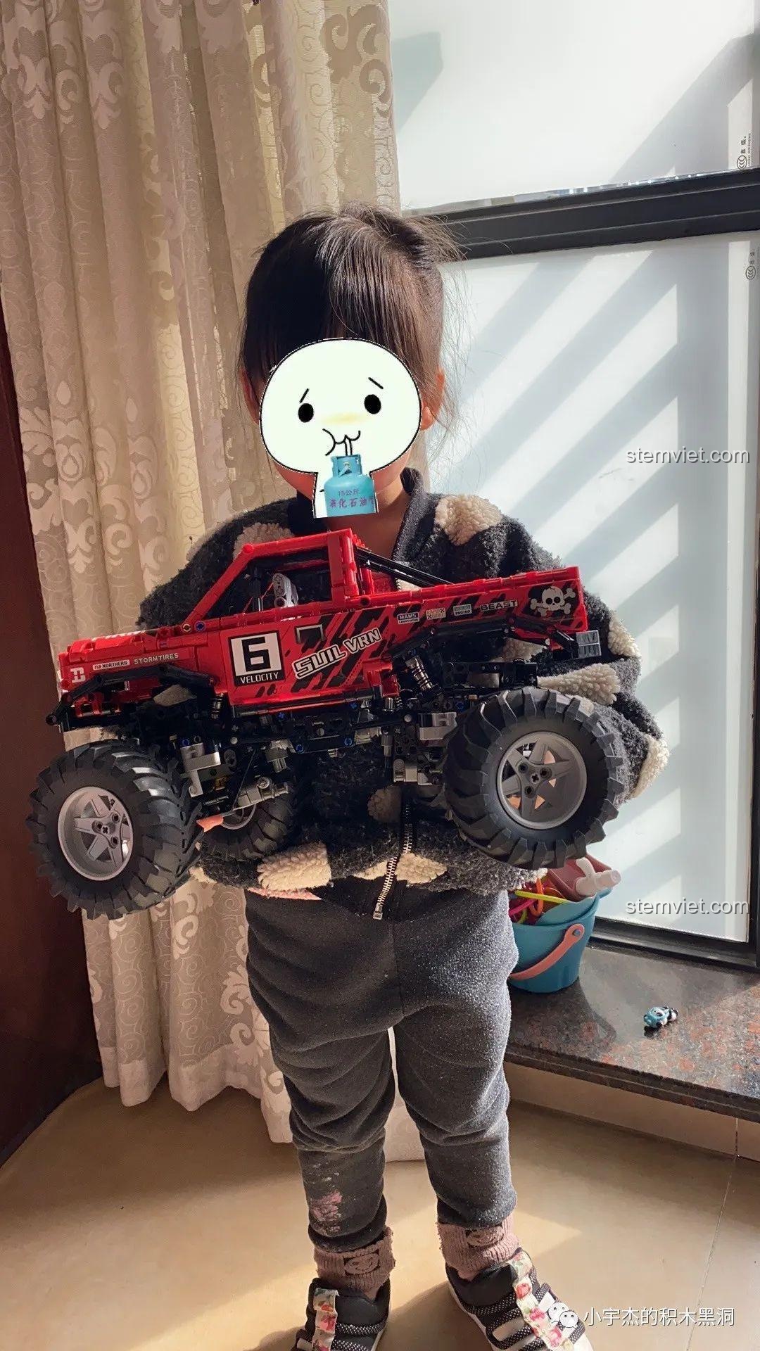 Một em bé đang cầm trên tay mô hình xe tải quái vật Happy Build XQ1212D, cho thấy kích thước lớn của sản phẩm.