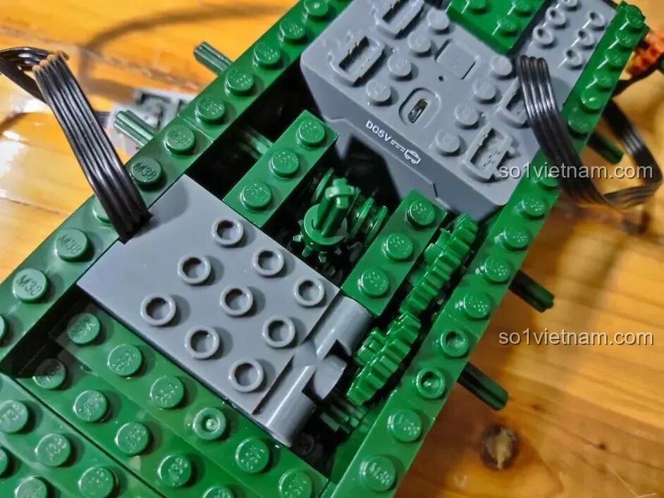 Cận cảnh việc lắp hộp pin màu xám vào giữa khung gầm xanh của xe tăng đồ chơi Sluban.