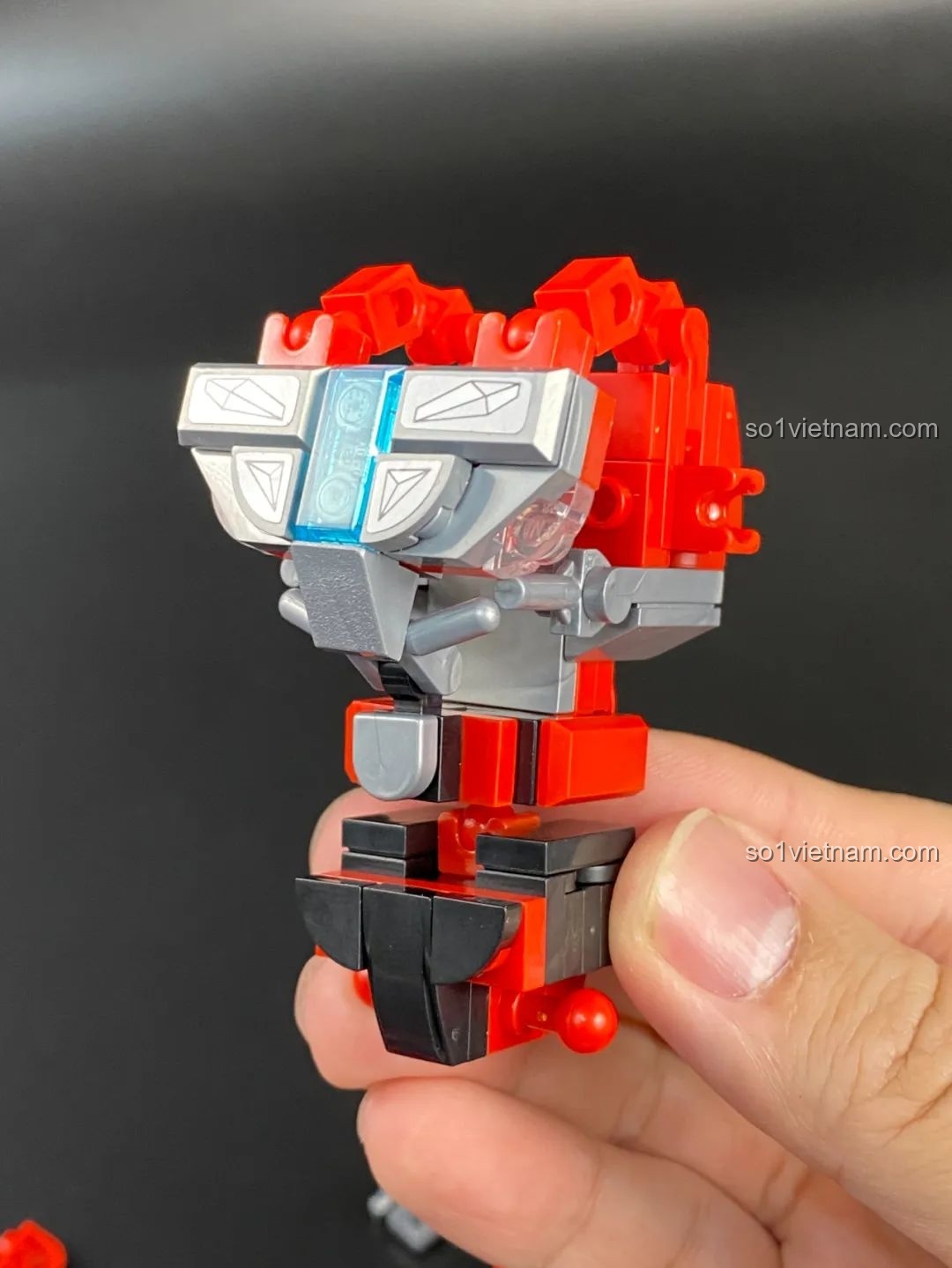 Một người đang lắp ráp phần ngực của Mecha Ultraman Geed Qman 75047, các chi tiết màu đỏ, bạc và xanh.