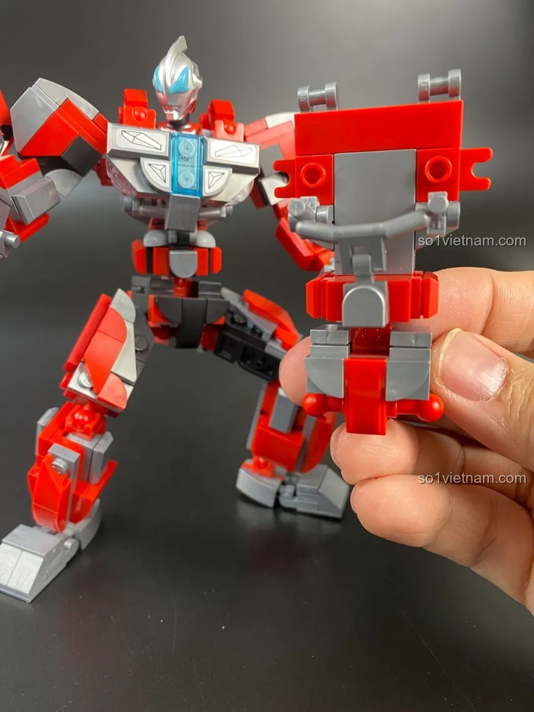 Một người đang cầm phần tay của Mecha Ginga đang lắp ráp dở, phía sau là mô hình gần hoàn thiện.