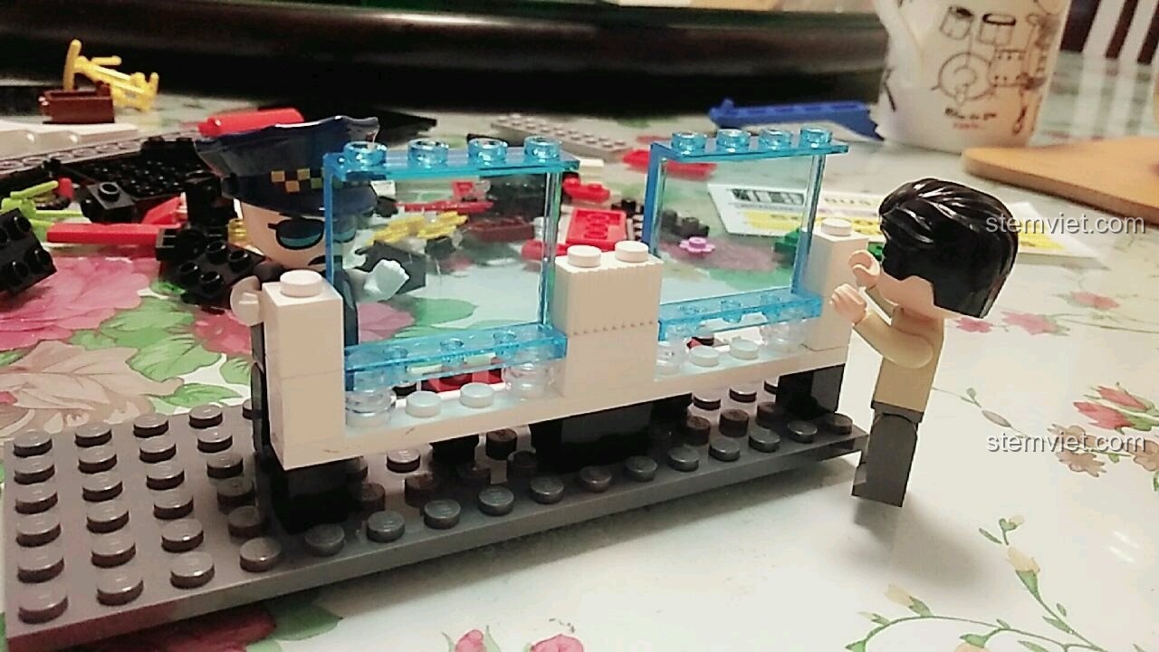 Bác tài xế đang lắp ráp phần khung và cửa sổ cho trạm chờ xe buýt trong bộ đồ chơi lắp ghép QMAN 1136.