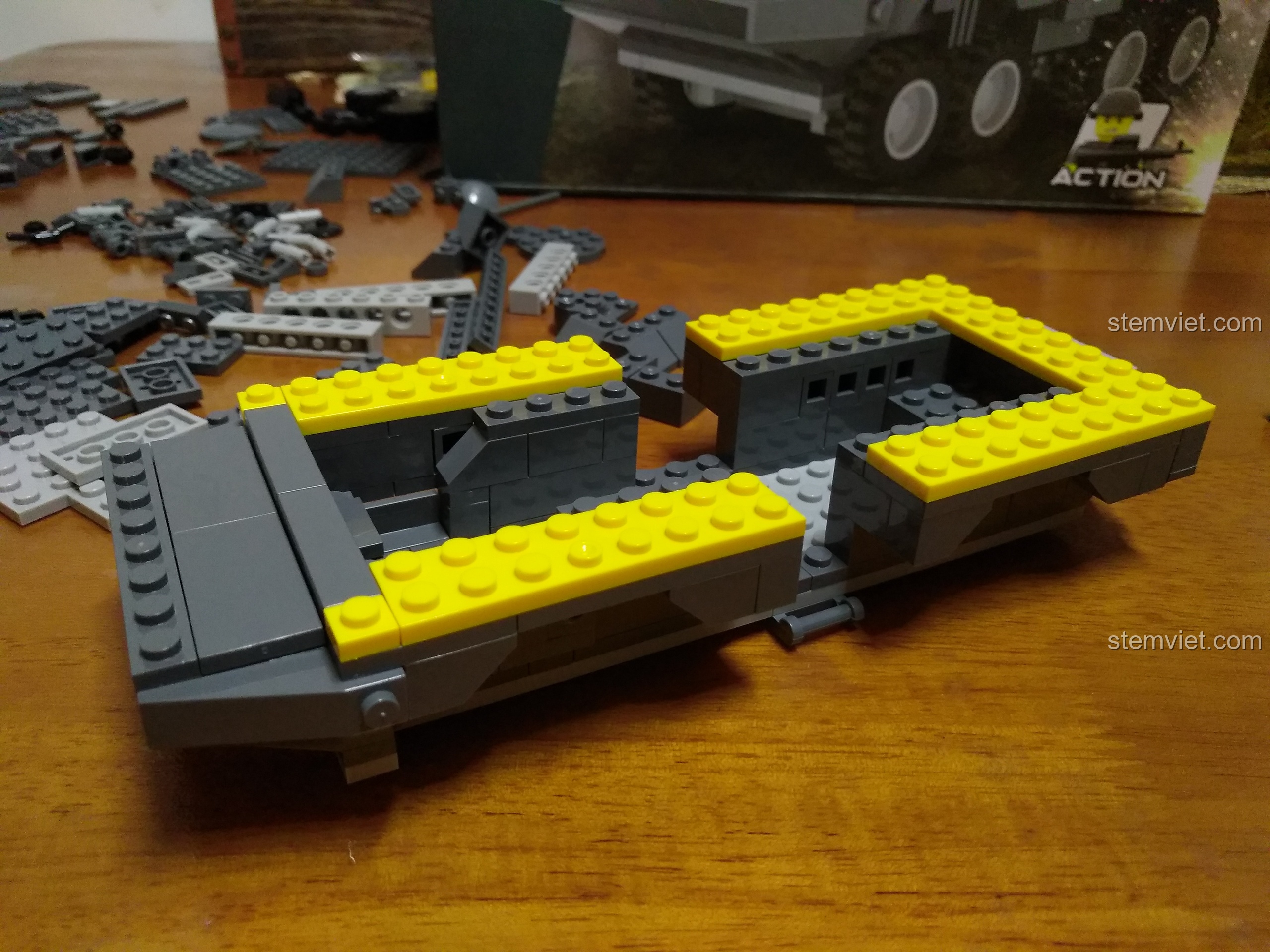 Bắt đầu lắp ráp phần khung gầm của bộ đồ chơi Xe Bọc Thép WANGE 3661, với các chi tiết màu xám và vàng nổi bật.