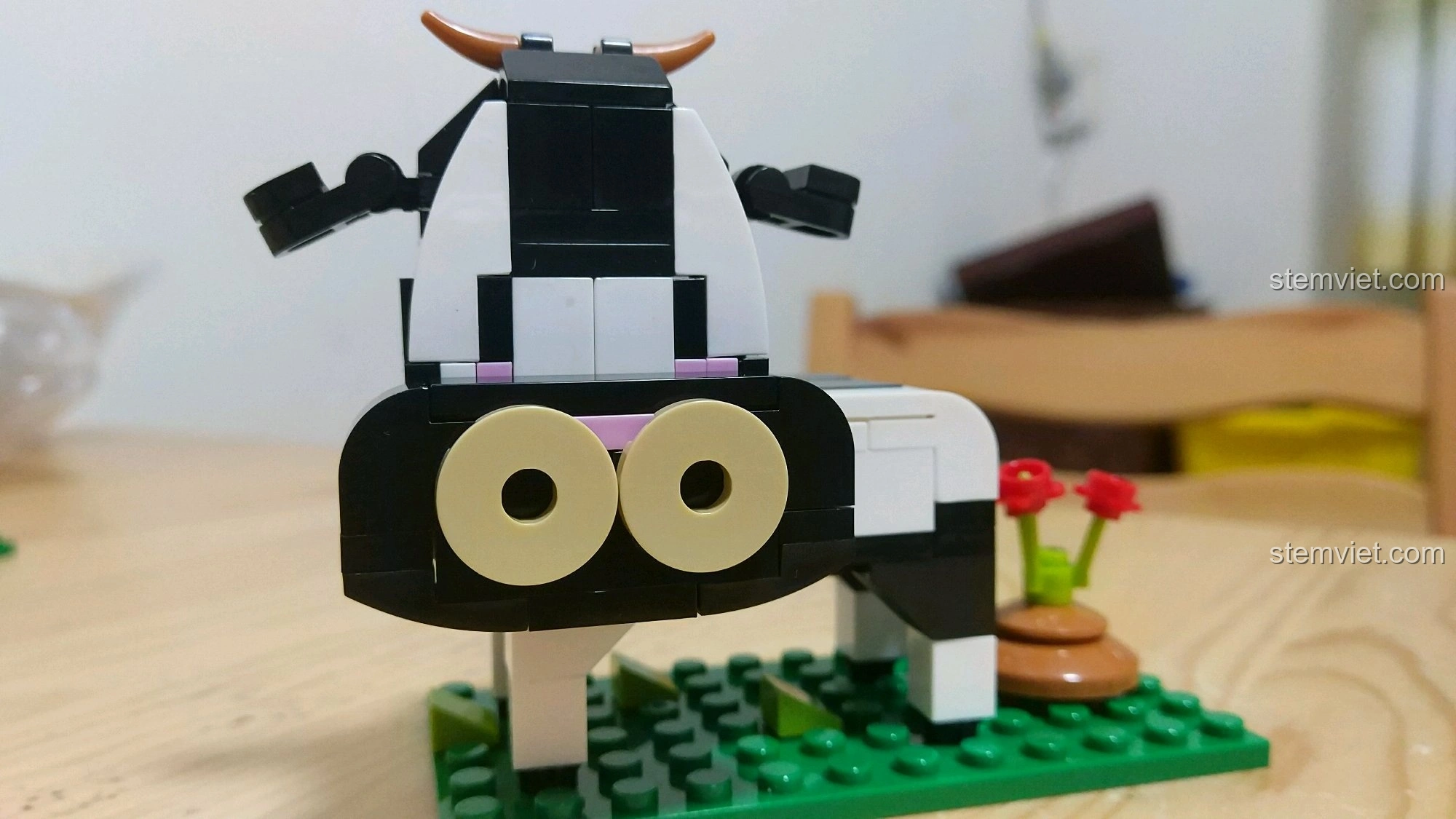 Mô hình Trâu Sửu màu đen trắng, đứng trên nền cỏ xanh, bên cạnh có một đống phân bò và hoa nhỏ, từ bộ lắp ráp 12 Con Giáp XINGBAO XB-18001.