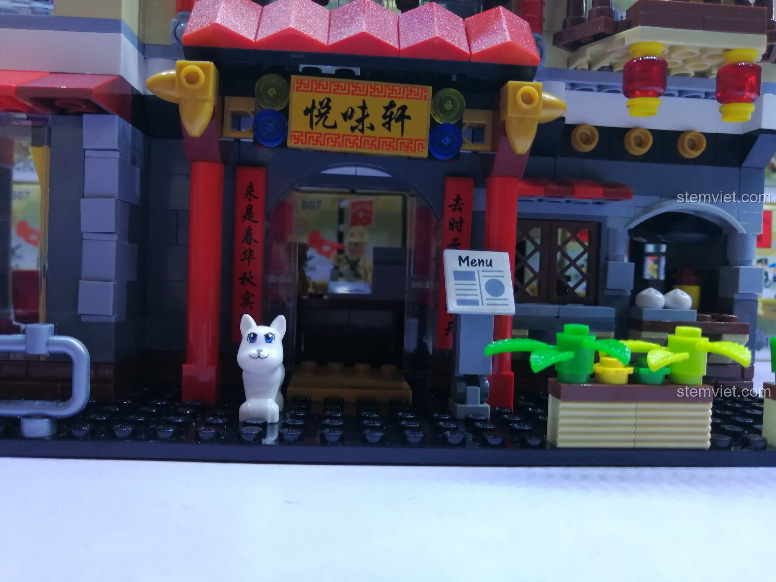 Mặt tiền tầng trệt của nhà hàng QMAN 1137 với cổng chào, biển hiệu, menu và một chú mèo trắng.