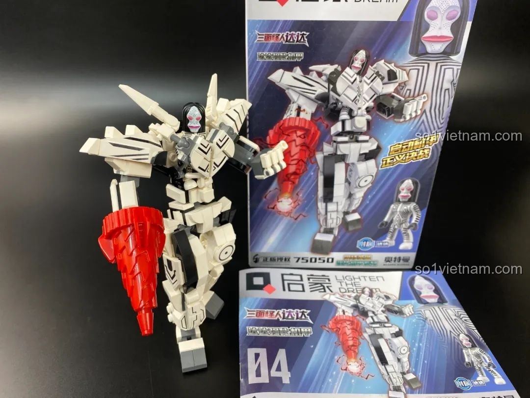 Mô hình Mecha Dada Qman 75050 đã hoàn thiện, đứng bên cạnh hộp và sách hướng dẫn.