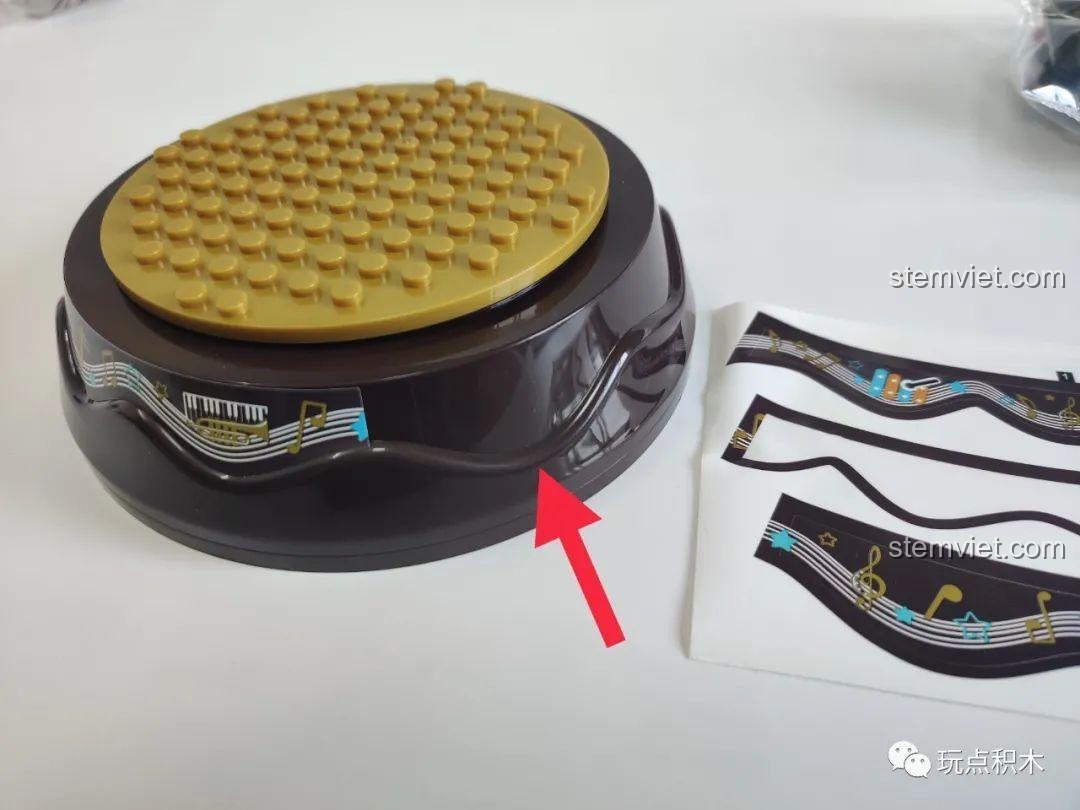 Hướng dẫn dán sticker trang trí cho đế hộp nhạc WOMA C0360, căn chỉnh theo đường lượn sóng có sẵn.