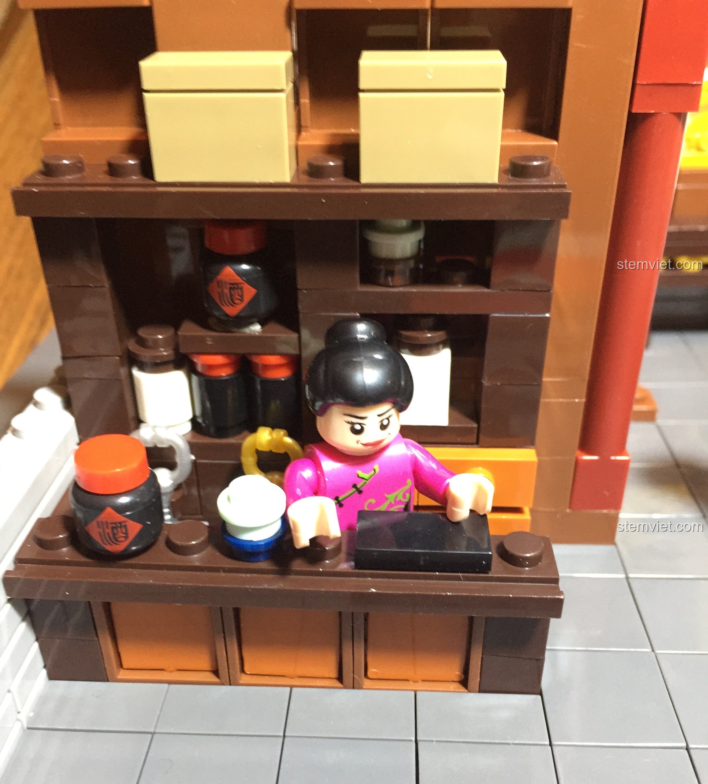 Minifigure bà chủ quán đứng sau quầy lễ tân, sẵn sàng phục vụ trong mô hình Vạn Phúc Khách Sạn.