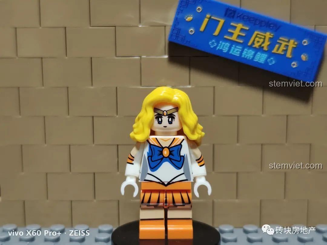 Minifigure Thủy Thủ Sao Kim Minako Aino chụp chính diện, nổi bật với mái tóc vàng bồng bềnh và trang phục màu cam.