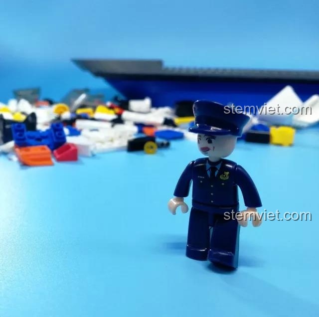 Minifigure thuyền trưởng tàu cảnh sát Sluban B0657 đứng trước các mảnh ghép chưa lắp ráp, chuẩn bị cho nhiệm vụ tuần tra biển.