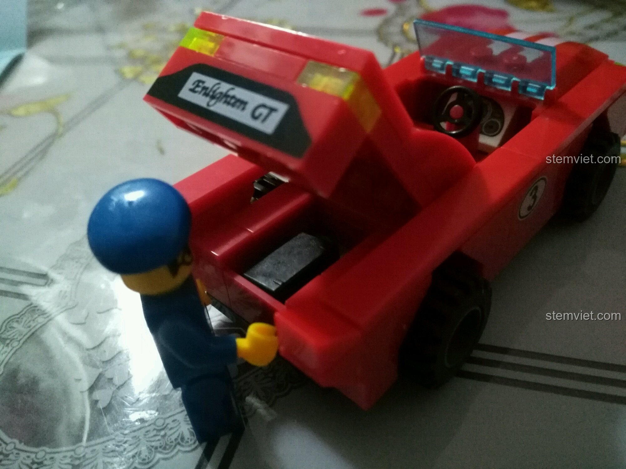 Minifigure đang đặt chiếc cặp vào cốp sau của xe đua Enlighten 402, tăng khả năng chơi.