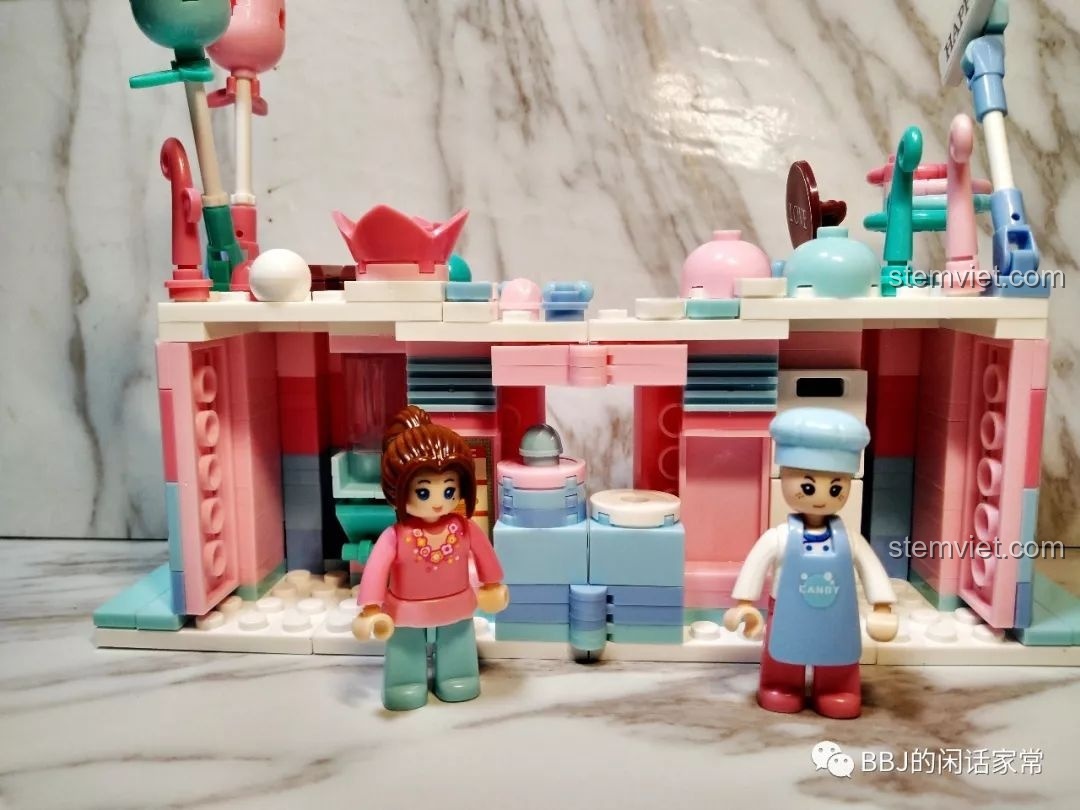 Hai minifigure thợ làm bánh và cô bé được đặt bên trong không gian mở của tiệm bánh Sluban B0705H.