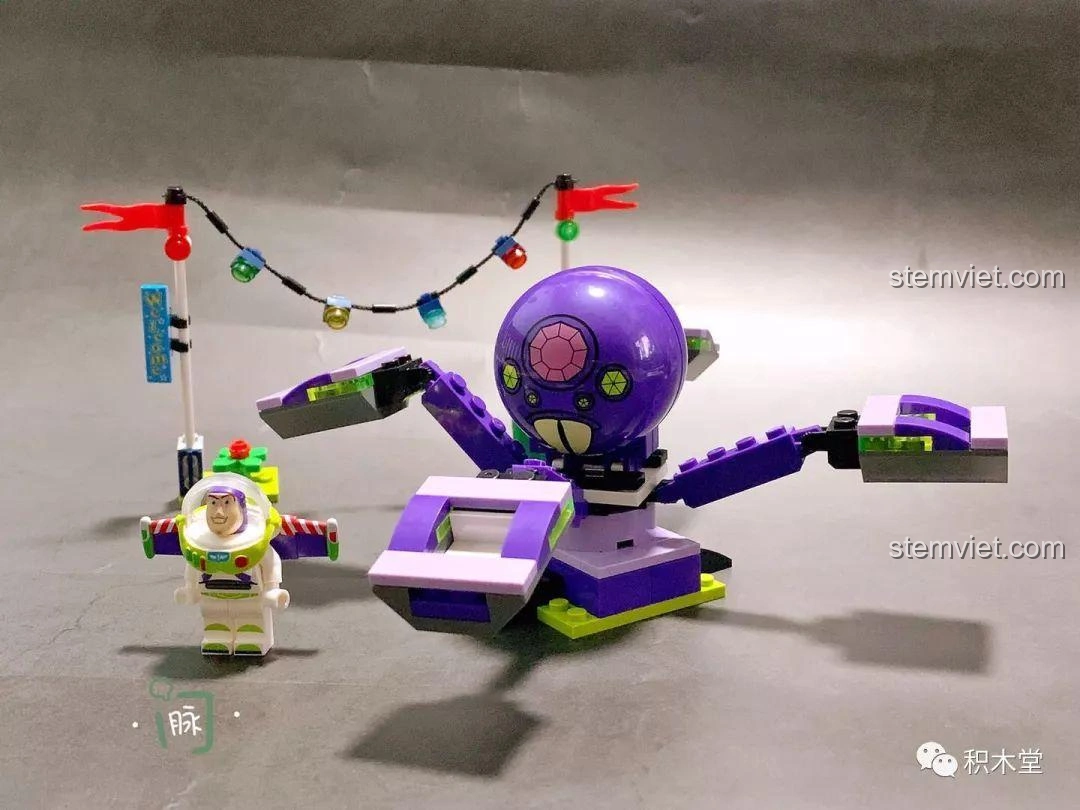 Mô hình hoàn chỉnh của Buzz Lightyear và cỗ máy bạch tuộc phun nước xoay tròn, với Buzz đứng cạnh và cờ trang trí.