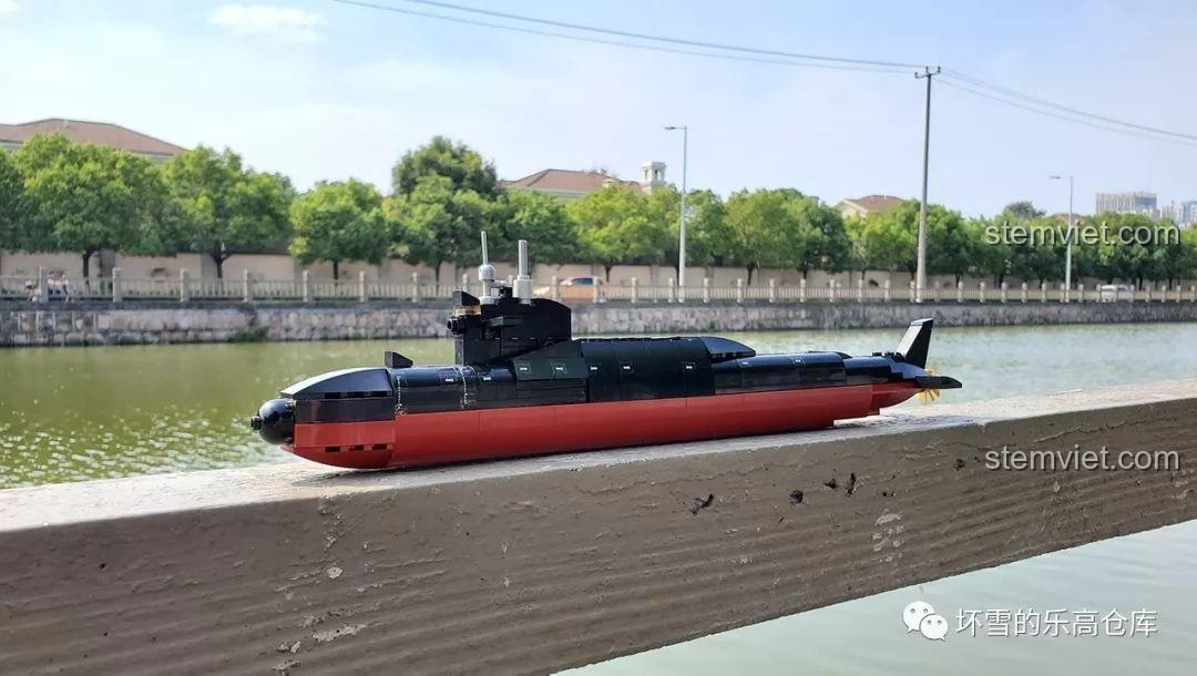 Mô hình tàu ngầm hạt nhân Sluban M38-B0703 đặt trên lan can gỗ cạnh dòng sông, thể hiện góc nhìn tổng thể của sản phẩm.