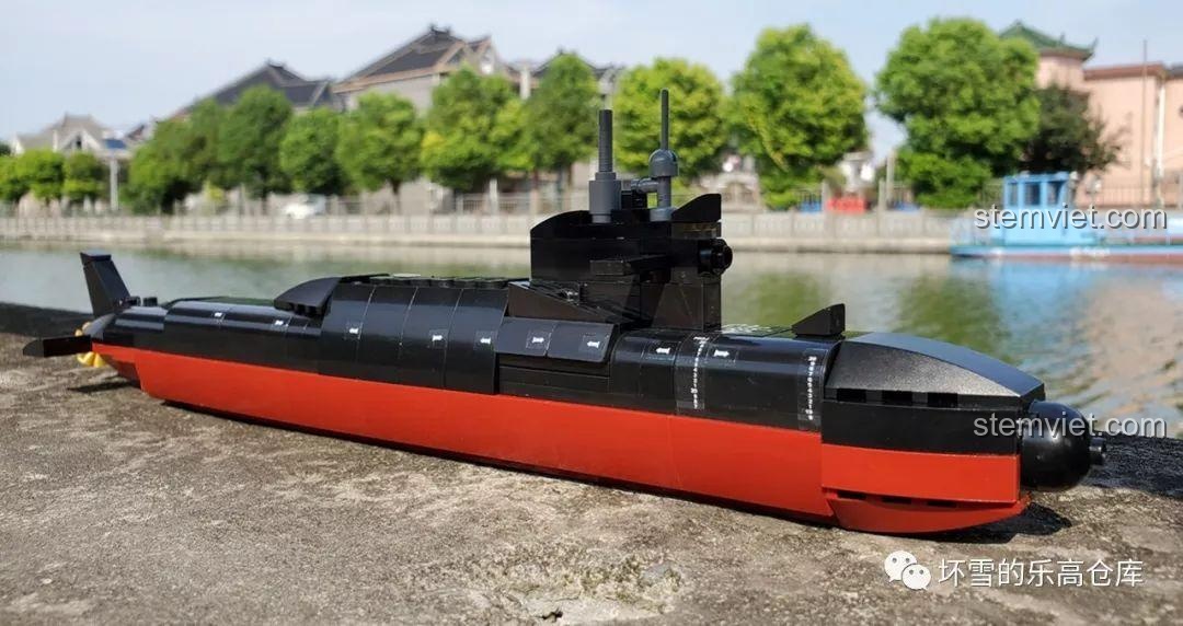 Toàn cảnh mô hình tàu ngầm hạt nhân Sluban M38-B0703 đã hoàn thành, đặt trên lan can gỗ với cảnh quan cây xanh phía sau.