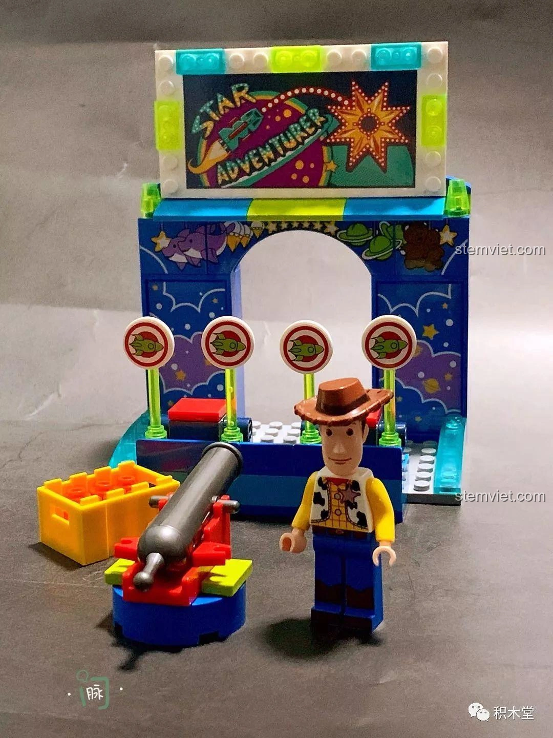 Mô hình Trò Chơi Bắn Bia của Woody hoàn chỉnh, với Woody đứng cạnh khẩu pháo và các mục tiêu bắn bia.