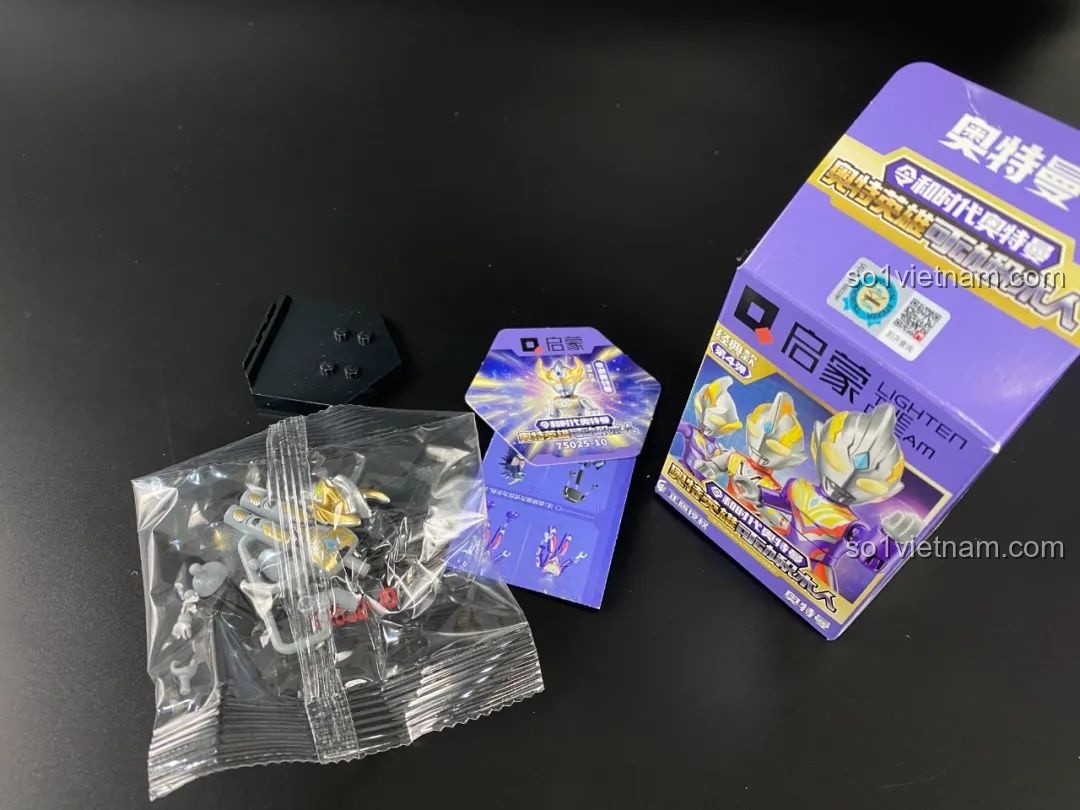 Mở một hộp blind box nhỏ, bên trong là túi chứa figure, thẻ bài và đế trưng bày.