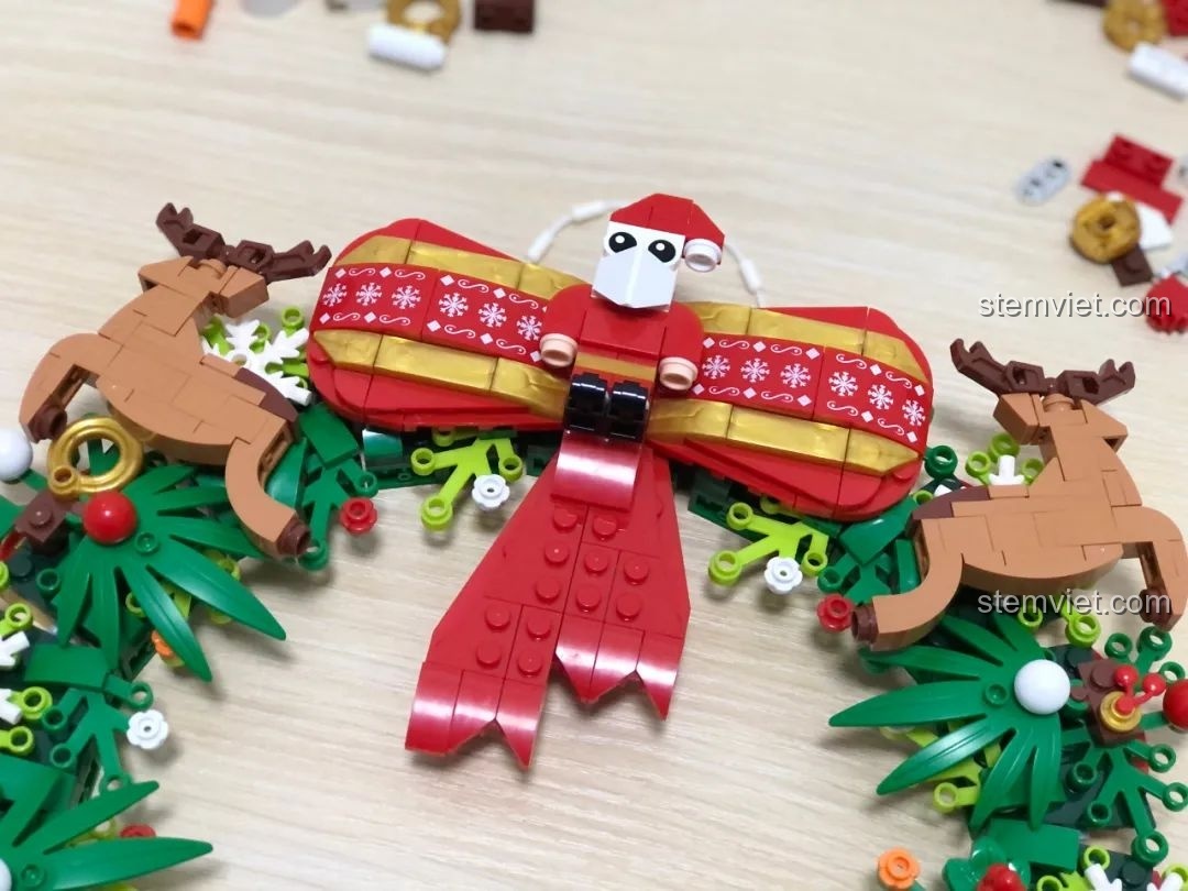Chiếc nơ lớn và hai chú tuần lộc trang trí trên bộ lắp ghép Vòng Hoa Giáng Sinh Đa Sắc JAKI JK5118, rất đáng yêu.