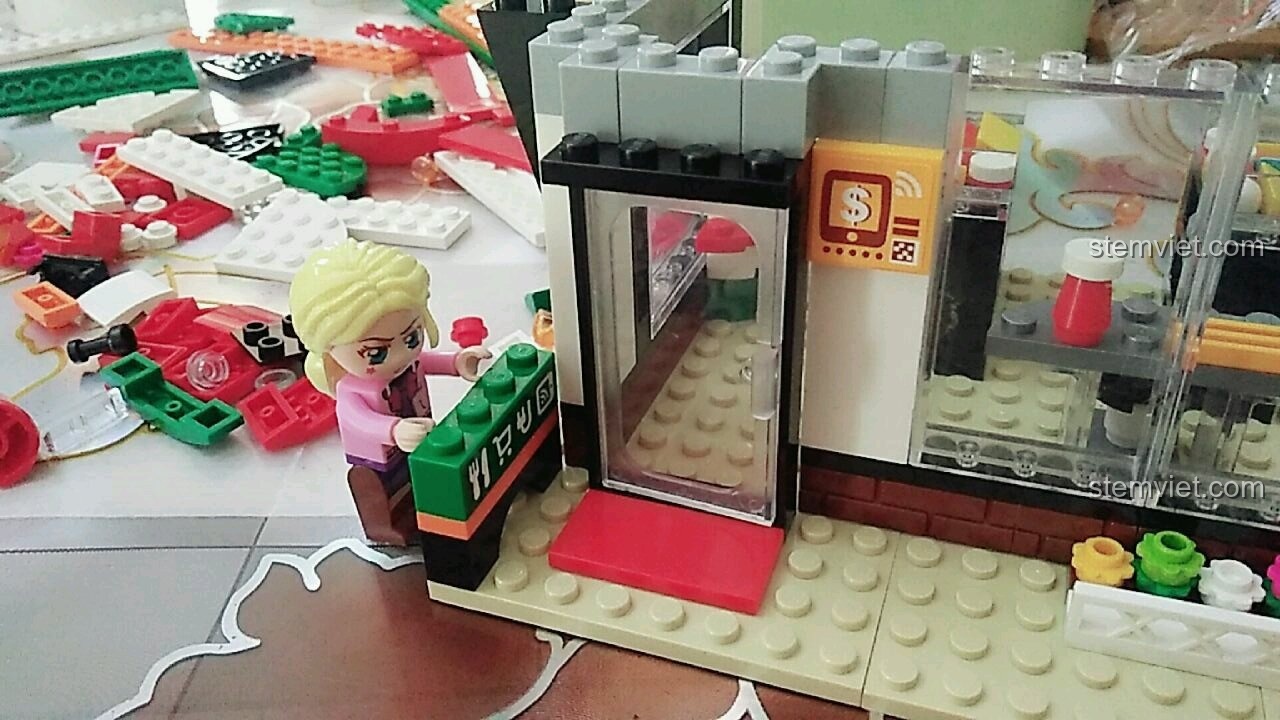 Minifigure cô chủ Tử Kỳ đang lắp đặt cánh cửa và biển hiệu 'Open' cho mô hình QMAN 1133 Cửa Hàng Tiện Lợi.