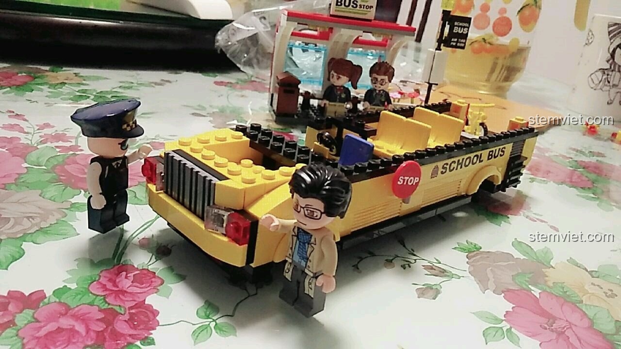 Các nhân vật học sinh đang ăn bánh trong khi chờ xe buýt đến, một cảnh chơi vui nhộn với bộ đồ chơi xếp hình QMAN 1136.