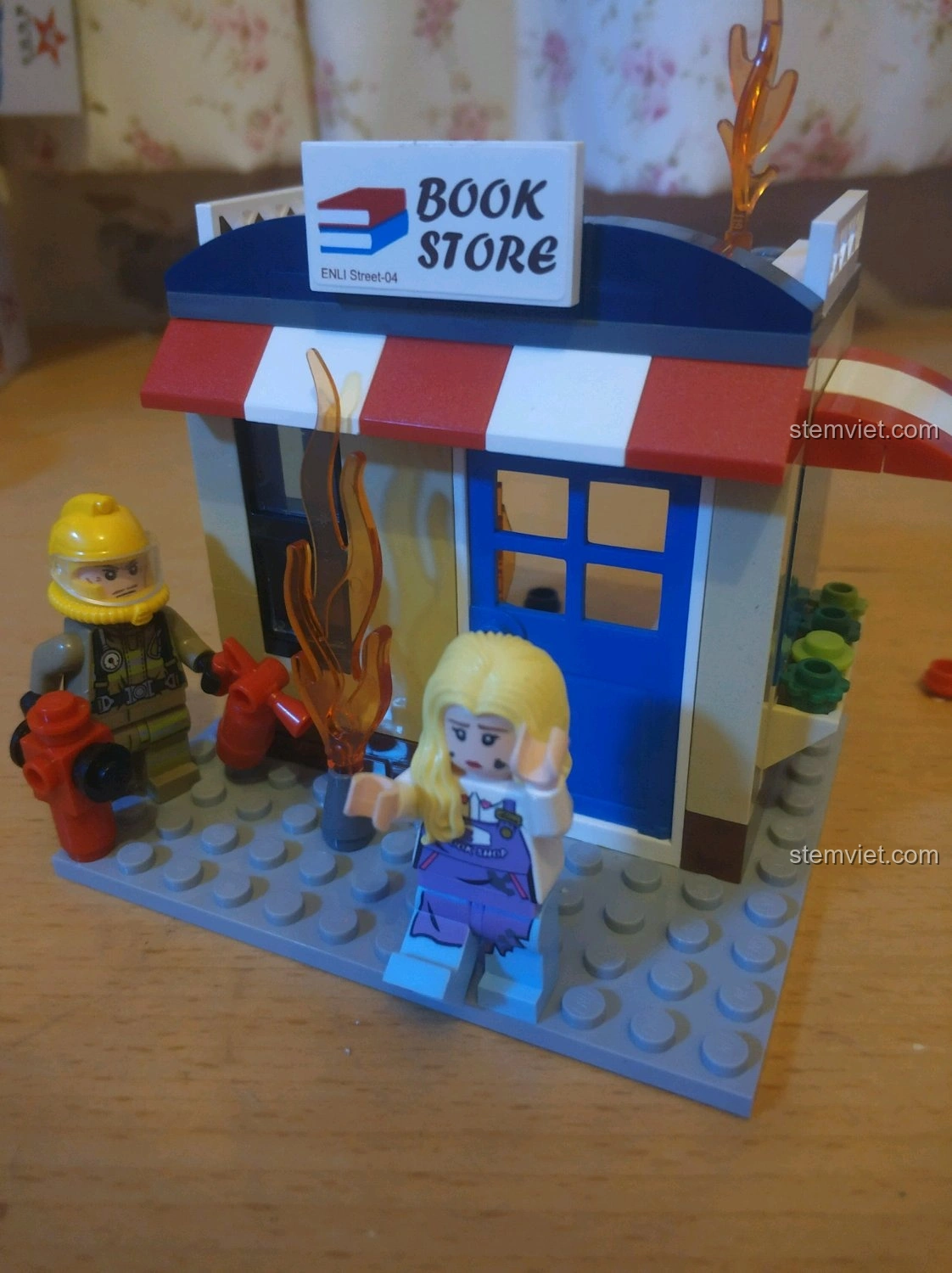 Cảnh lính cứu hỏa và nhân viên nhà sách tương tác với mô hình nhà sách đang cháy QMAN 2804, tạo nên câu chuyện.