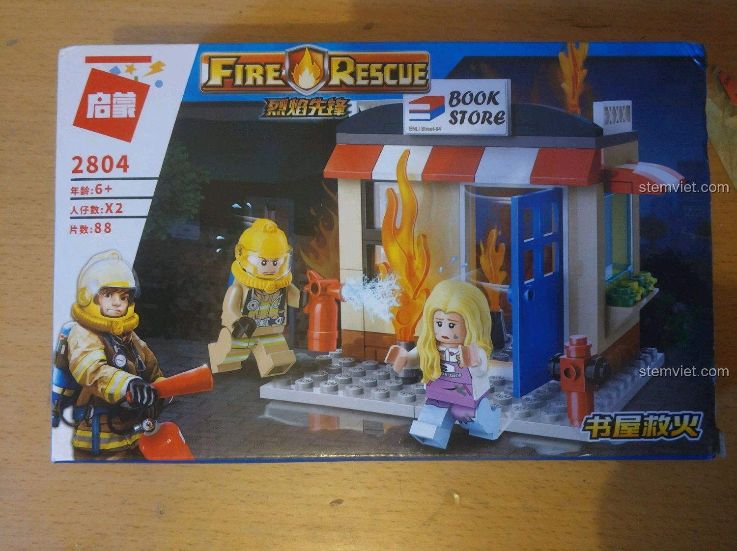 Hộp sản phẩm bộ lắp ráp QMAN 2804 Cứu Hỏa Nhà Sách với hình ảnh lính cứu hỏa và nhà sách đang cháy, thu hút bé trai 6 tuổi.