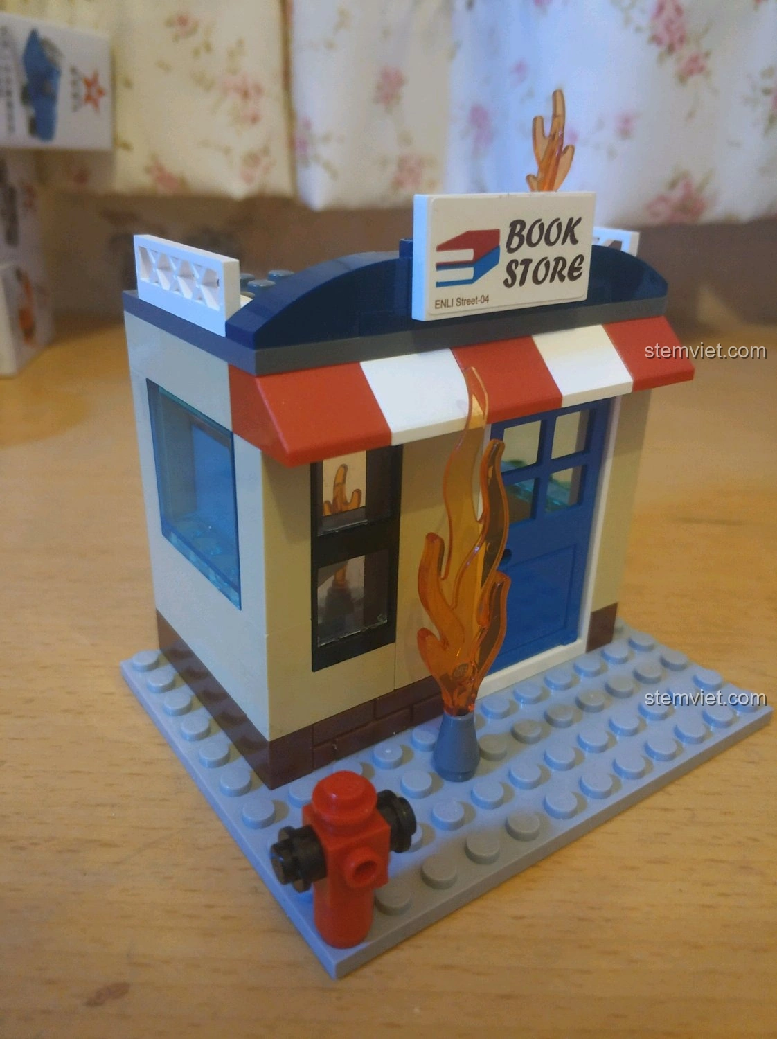 Mô hình nhà sách đang cháy QMAN 2804 nhìn từ một bên, với các chi tiết ngọn lửa và vòi cứu hỏa.