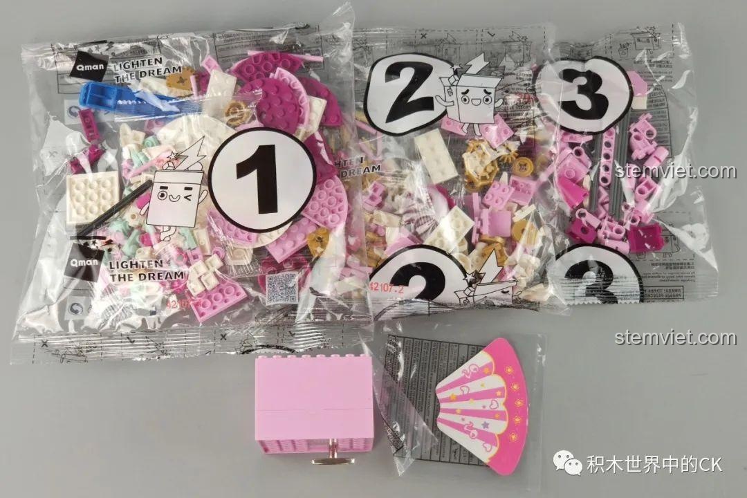 Các túi mảnh ghép được đánh số và hộp nhạc màu hồng của Hộp nhạc đu quay QMAN.