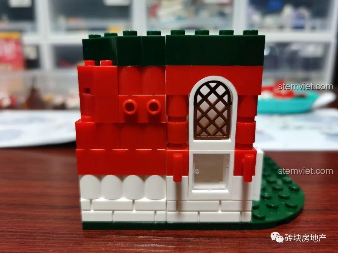 Một phần tường của mô hình Hộp nhạc Giáng Sinh Zhe Gao QL0981, với cửa sổ và các chi tiết trang trí màu đỏ và xanh.