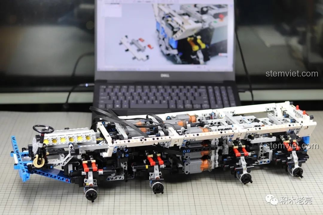 Khung gầm xe tải Mould King 13144 Tatra T813 8x8 PROFA đang trong quá trình lắp ráp, với laptop hiển thị hướng dẫn phía sau.