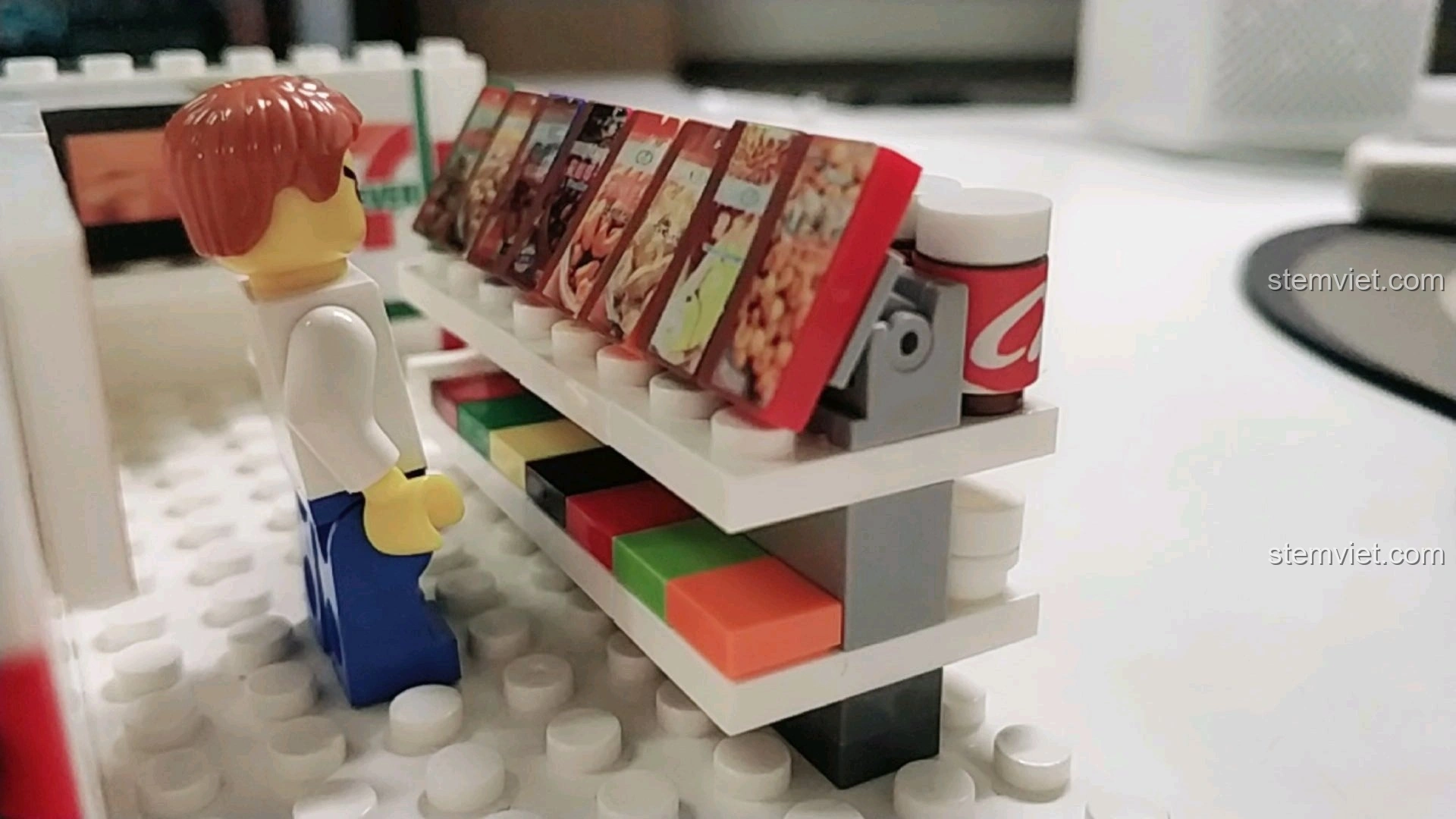 Minifigure đang xem các gói snack trên kệ hàng trong mô hình cửa hàng tiện lợi 7-Eleven.