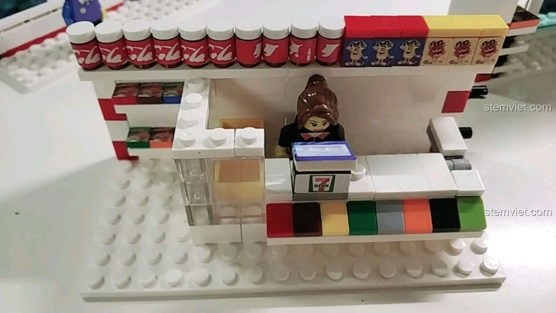 Chi tiết quầy thu ngân với máy tính tiền và minifigure nhân viên trong mô hình cửa hàng tiện lợi 7-Eleven.