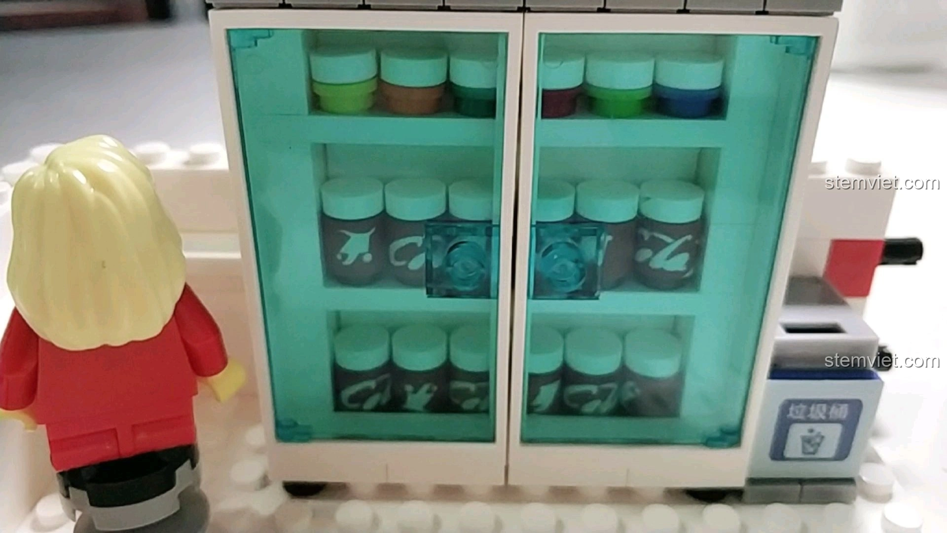 Tủ lạnh chứa đầy đồ uống trong mô hình cửa hàng tiện lợi 7-Eleven, với minifigure đứng cạnh.
