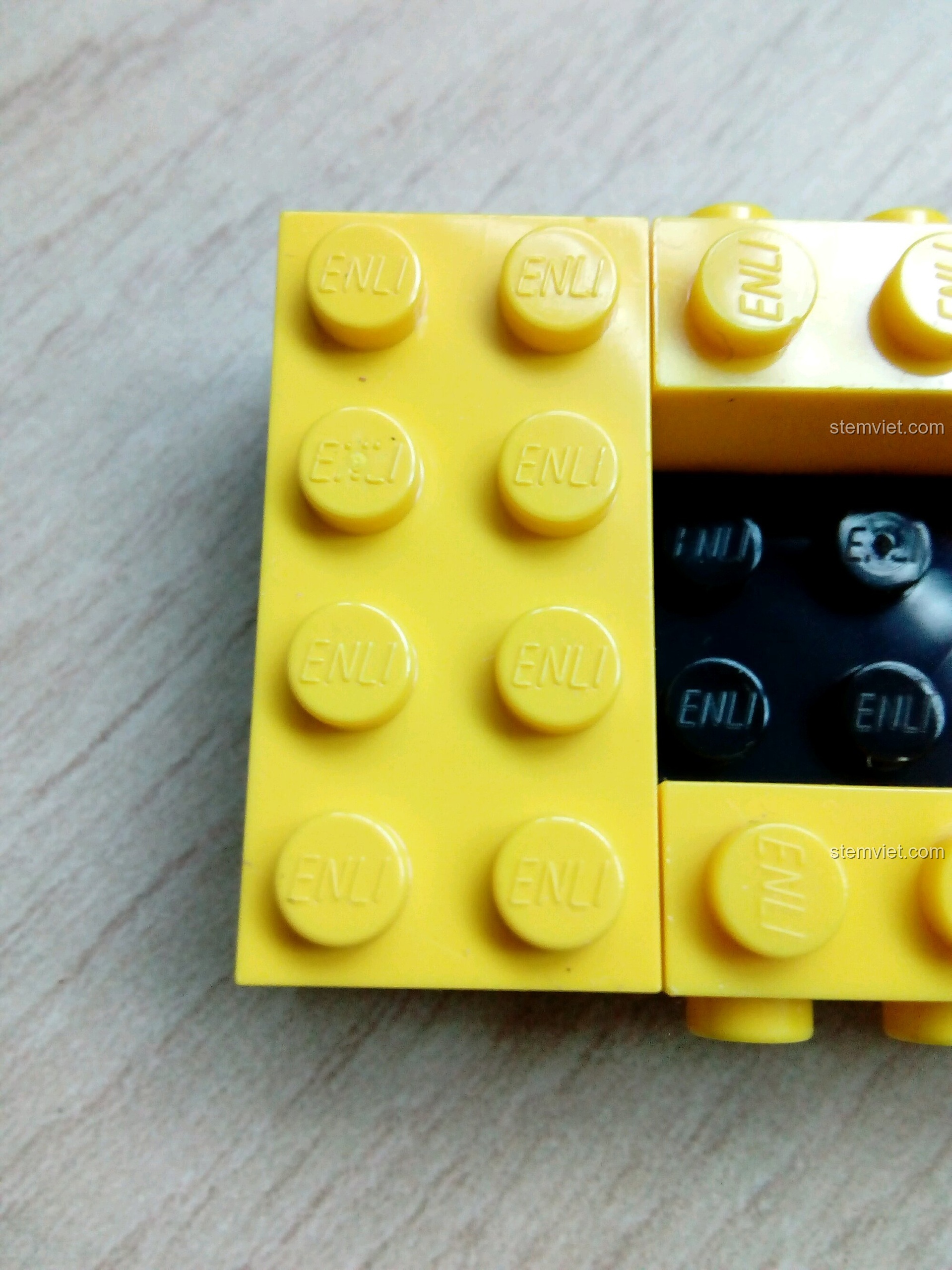 Cận cảnh chi tiết gạch lắp ráp màu vàng với logo 'ENLI' của hãng Enlighten, chứng minh chất lượng bộ Tàu Ngầm Quan Sát Cá Heo 1215. Cảm nhận QMAN 1215 Tàu Ngầm Quan Sát Cá Heo.