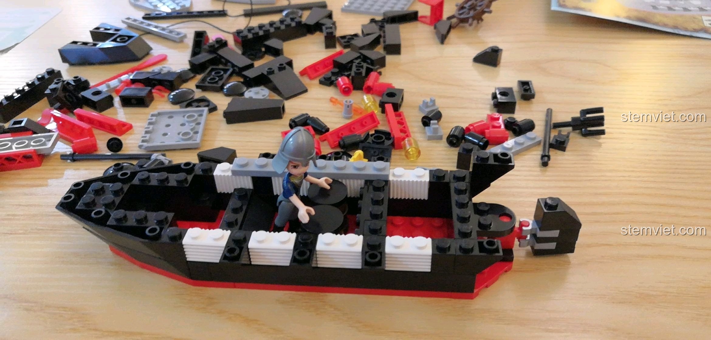 Một minifigure đang cầm bản đồ kho báu, bên cạnh là phần thân tàu Tàu Hải Tặc Barbara 301 đang dần thành hình.