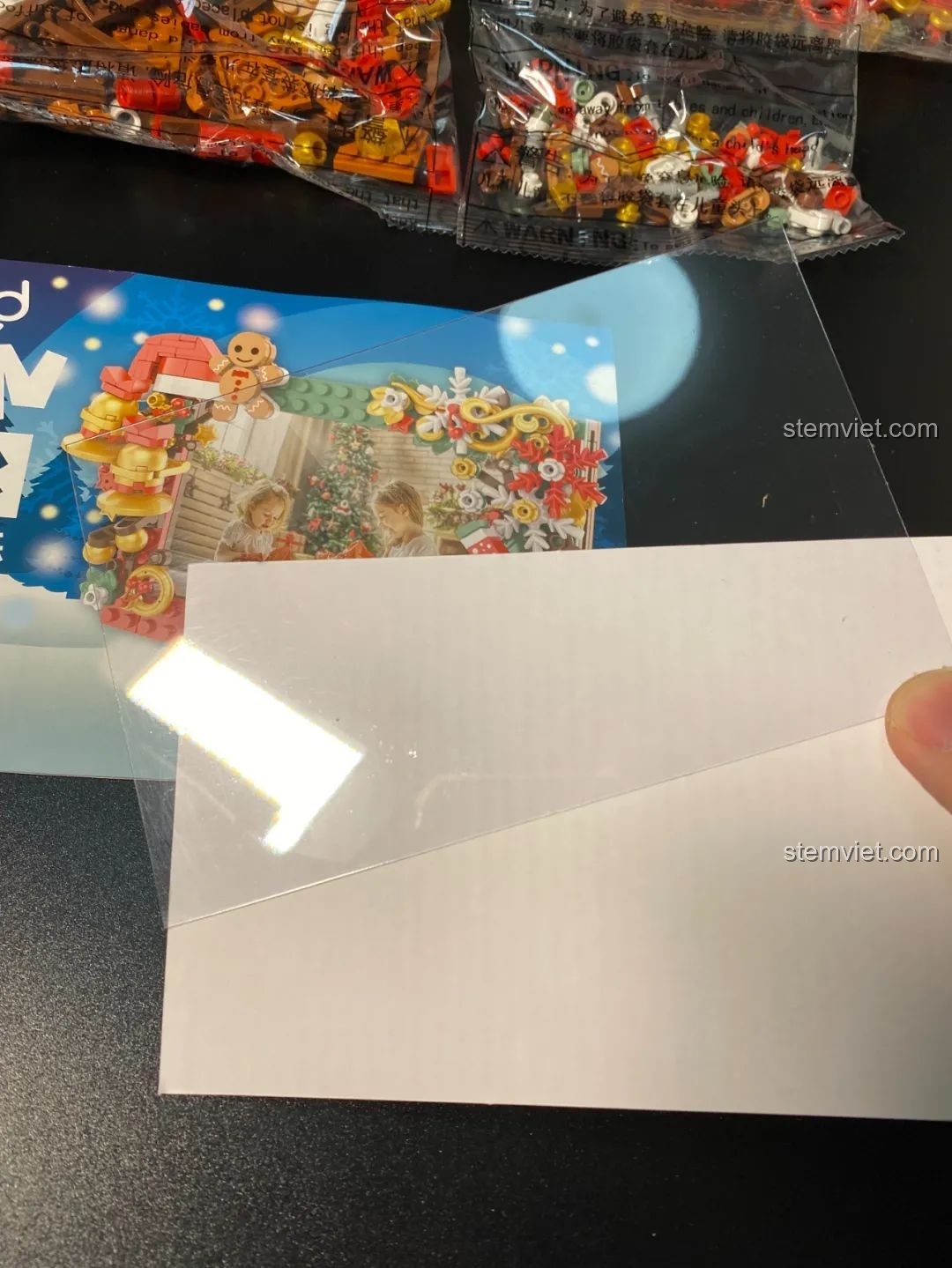 Các linh kiện bên trong hộp đồ chơi lắp ráp JAKI JK5107 Khung Ảnh Giáng Sinh, bao gồm tấm phim nhựa và bìa cứng.